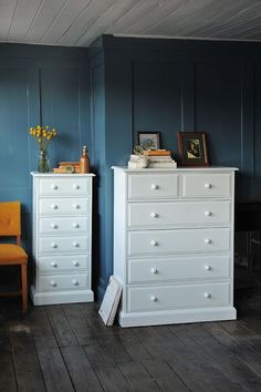 a white dresser sitting next to a chair in a blue room with wood flooring