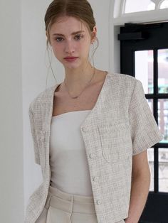 This product is a sophisticated blouse crafted in a tweed fabric, offering both texture and a touch of elegance to the wearer. The piece features a classic collar and is adorned with a set of coordinating buttons, providing a seamless look that is perfect for professional settings or everyday chic. Its short sleeves and tailored fit bring a modern twist to the traditional tweed aesthetic. - The blouse’s tailored fit accentuates the body's silhouette while maintaining a comfortable range of movement.- Short sleeves add a contemporary and casual element to the otherwise formal tweed fabric.- Coordinating buttons down the front lend a cohesive and polished finish to the design.- The classic collar rounds off the blouse's design, making it a versatile piece that can be dressed up or Chic Beige Tweed Jacket With Buttons, Elegant Tweed Jacket With Button Closure For Business Casual, Elegant Beige Tweed Jacket For Office, Elegant Business Casual Tweed Jacket With Button Closure, Elegant Beige Tweed Office Jacket, Spring Elegant Tweed Jacket With Hidden Buttons, Elegant Button-up Tweed Jacket For Office, Elegant Fitted Button-up Tweed Jacket, Elegant Fitted Tweed Button-up Jacket