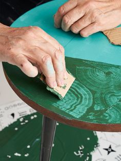 a person is using a sponge to paint a table with green and white designs on it