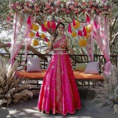 a woman in a pink and gold dress standing under a canopy with flowers on it