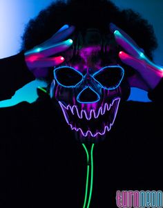 a person wearing a neon mask and holding their hands up to their face