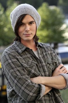 a young man with his arms crossed wearing a hat