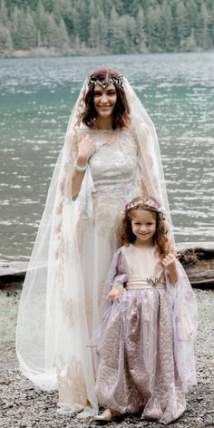 two brides standing next to each other on the shore of a body of water