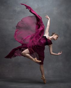 a woman in a purple dress is dancing with her arms spread out and legs extended