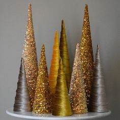 three gold and silver trees are sitting on top of a wooden table with glittery tops