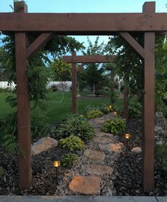 a wooden arbor with lights on it in the middle of a garden area at dusk