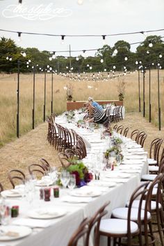 a long table set up with white plates and silverware for an outdoor dinner party