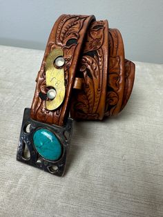 Very unusual vintage belt , or I should say it's an unusual buckle on a stylish tooled leather belt.  It has "BJ" engraved in a brass piece, and what looks to be a large turquoise stone set into the buckle. I believe the buckle is likely brass, but it looks silver in color.  It's one of a kind for sure.  In great shape, no flaws to note.  Sorry I don't know much more about it really.  ✏️✏️✏️DETAILS✏️✏️✏️ Brand: hand made Size on tag: - Fits like: small men's 31  Color:  2 tone brown with silver, Vintage Turquoise Belt With Concho, Western Antique Belt Buckles For Festival, Vintage Adjustable Belt Buckles For Rodeo, Vintage Adjustable Turquoise Belt, Adjustable Vintage Turquoise Belt, Adjustable Turquoise Vintage Belt, Vintage Leather Belt Buckles For Western-themed Events, Vintage Belt Buckles For Western-themed Events, Vintage Handmade Brown Belt Buckles