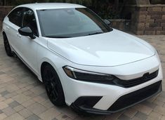 a white car parked in front of a brick wall