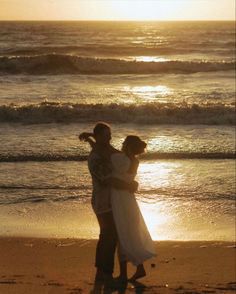 a man and woman hugging on the beach at sunset