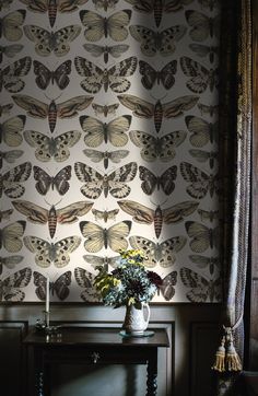 a vase with flowers on top of a table in front of a butterfly wallpaper