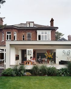 some people are sitting at a table in front of a large house with lots of windows