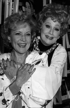 two women standing next to each other in front of bookshelves