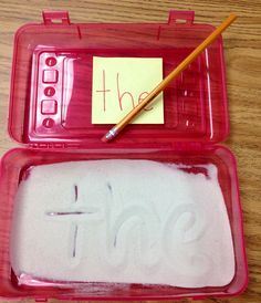 a red plastic container with writing on it and a pencil in the box next to it