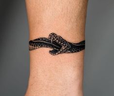 a black and white tattoo on the ankle of a man with a snake in it