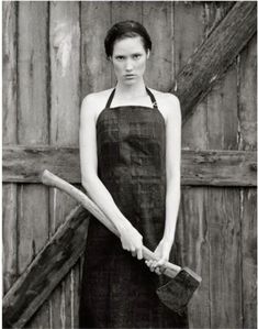 black and white photograph of a woman in an apron holding two large wooden sticks next to a barn door