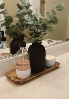 a bathroom counter with two black bottles and a candle on the tray next to it