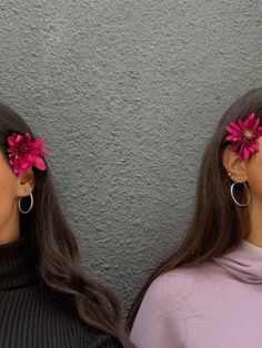 two women with pink flowers in their hair, one wearing a black turtle neck sweater