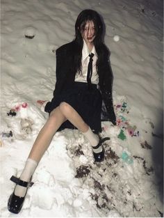 a woman sitting in the snow with her legs crossed and wearing high heels, black jacket and white shirt