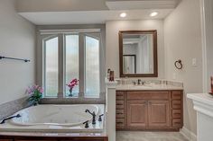 a large bath tub sitting next to a bathroom sink under a window with an open door