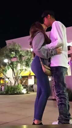 a man and woman kissing in front of a building at night with the lights on