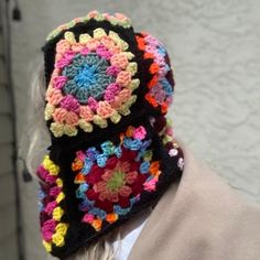 a woman wearing a multicolored crocheted hat with flowers on the brim