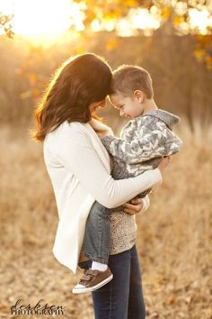 a woman holding a boy in her arms while the sun is setting behind them,