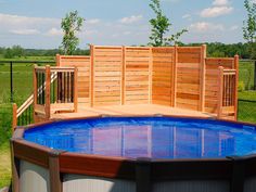 an above ground swimming pool surrounded by wooden fenced in area with green grass and trees