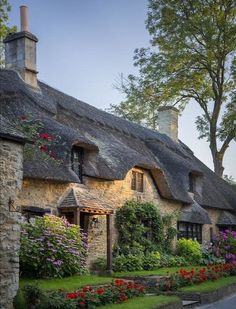 an old english country house with flowers in the front yard and thatched roof windows