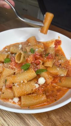 a white bowl filled with pasta and sauce on top of a wooden table next to a fork