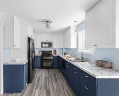 a kitchen with blue and white cabinets, wood flooring and stainless steel appliances in it