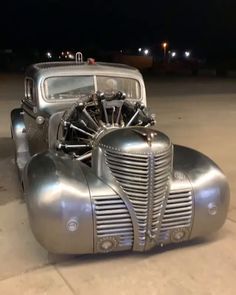 an old silver car parked on top of a parking lot next to a building at night