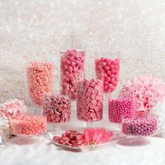 pink and white candies are arranged in glass containers on a table with other candy