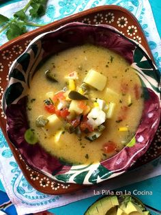 there is a bowl of soup with vegetables in it on the table next to an avocado