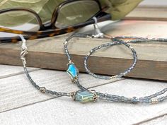 Bohemian and sophisticated in rainbow gray tones featuring blue cubic zirconia charms and silver plated crystal seed beads.  Shiny and and so elegant, this handmade eyeglass necklace will definitely create a unique look. This eyeglass lanyard is made on strong quality beading wire with wire guardians that protect the quality white eyeglass holder grips. The necklace is ended with spring clasps that hold the eyeglass grips and they can be easily removed to transform the necklace into a mask holde Silver Glass Beaded Necklaces With Spacer Beads, Silver Glass Beaded Necklaces With Faceted Beads, Silver Glass Beaded Necklace With Spacer Beads, Silver Beaded Necklace With Faceted Glass Beads, Silver Glass Beaded Necklace With Faceted Beads, Spiritual Silver Glass Beaded Necklaces, Spiritual Silver Beaded Necklaces, Eyeglass Necklace, Grandma Necklace