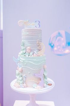 a three tiered cake sitting on top of a white table next to a purple wall