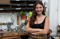 a woman standing in front of a workbench with her arms crossed and looking at the camera