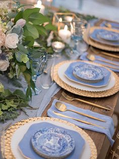 the table is set with blue and white plates, silverware, flowers and candles