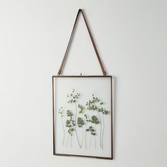 a white wall hanging with some plants on it's side and a brown frame