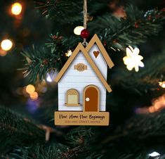 a christmas ornament hanging from a tree with lights in the background and an ornament that says new home, new beginnings