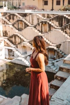 a woman in a red dress is standing on some steps and looking at the water