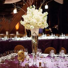 a tall vase filled with white flowers sitting on top of a purple table cloth covered table