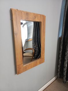 a mirror that is on the side of a wall near a chair and window with curtains