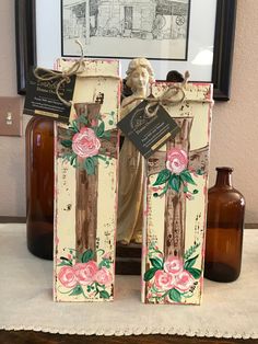 two wooden blocks decorated with pink roses and an angel statue are on a table next to some brown bottles