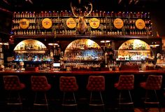 a bar with several stools and many bottles on the wall behind it in a dimly lit room