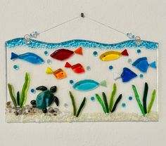 a colorful glass wall hanging with fish and seaweed on it's bottom half