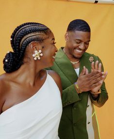 a man and woman standing next to each other in front of an orange wall smiling