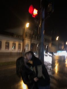 a man and woman kissing on the street at night with traffic lights in the background