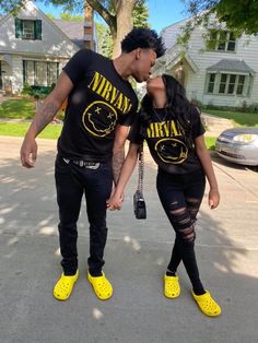 a man and woman standing next to each other in front of a house with yellow shoes