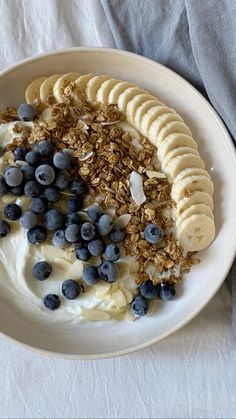 a white plate topped with yogurt and banana slices next to blueberries and granola